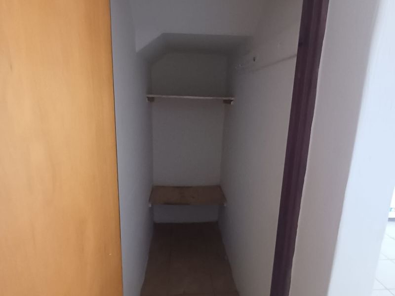 A small, empty utility or storage closet featuring tiled flooring and built-in shelving, suitable for additional household storage.