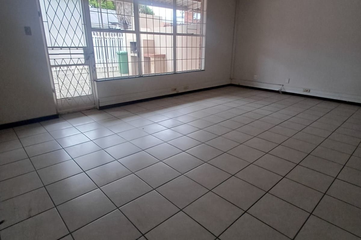 An empty, open-plan living area featuring tiled flooring, a security gate, and large windows providing natural light.