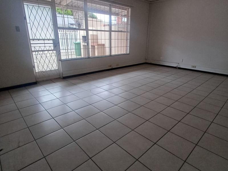 An empty, open-plan living area featuring tiled flooring, a security gate, and large windows providing natural light.