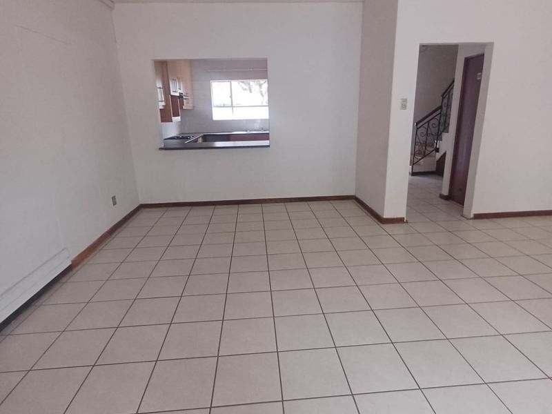 An empty open-plan living area featuring neutral tiled flooring and a convenient pass-through window connecting to the kitchen space.