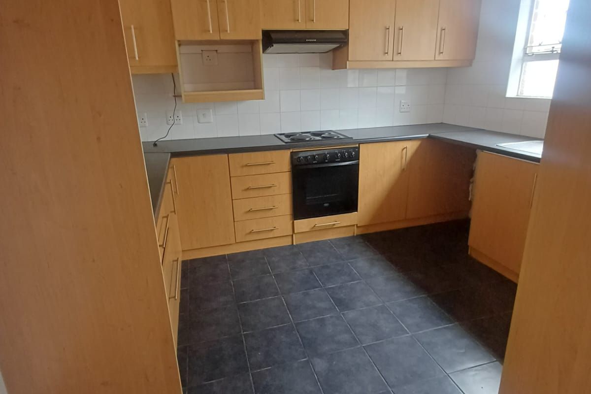 A functional kitchen featuring light wood-look cabinetry, dark tiled flooring, built-in oven, electric hob, and extractor fan with ample storage space.
