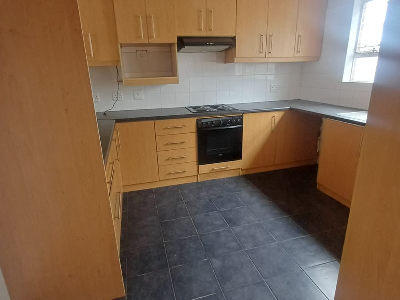 A functional kitchen featuring light wood-look cabinetry, dark tiled flooring, built-in oven, electric hob, and extractor fan with ample storage space.