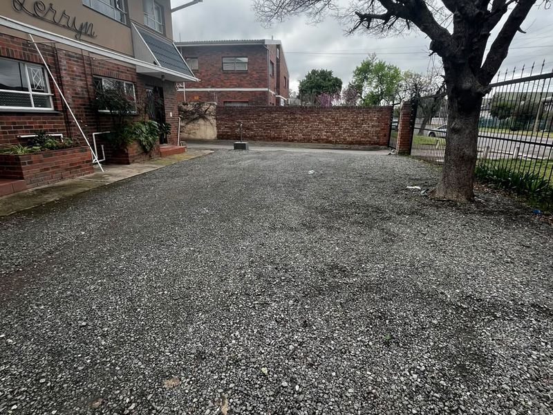 Front exterior view of the apartment building featuring a gravel driveway, brick facade, and secure perimeter fencing.