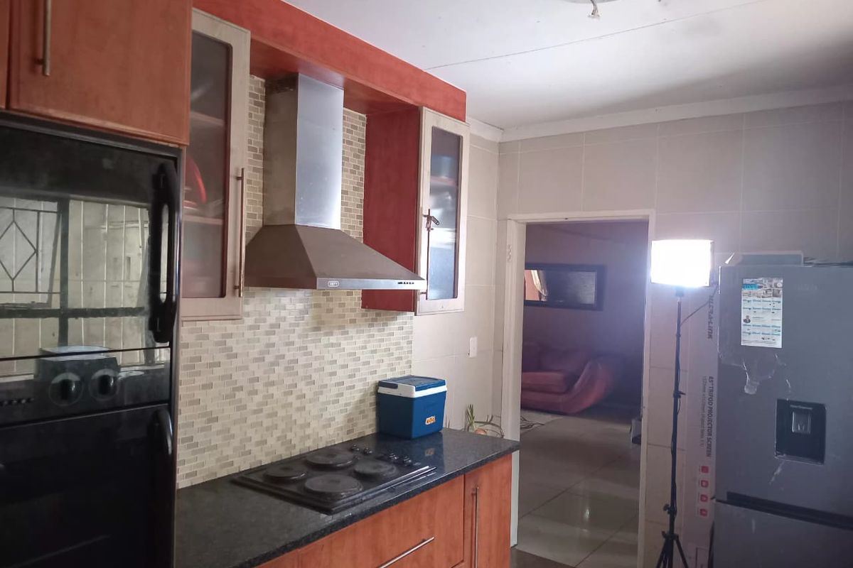 A functional kitchen featuring wood-finish cabinetry, granite countertops, a tiled backsplash, and a stainless steel extractor fan, with direct access to the living area.