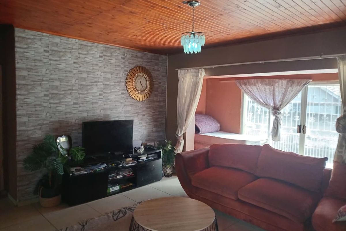 A living room featuring a timber tongue and groove ceiling, tiled flooring, and a stone-effect feature wall with access to an outdoor area.
