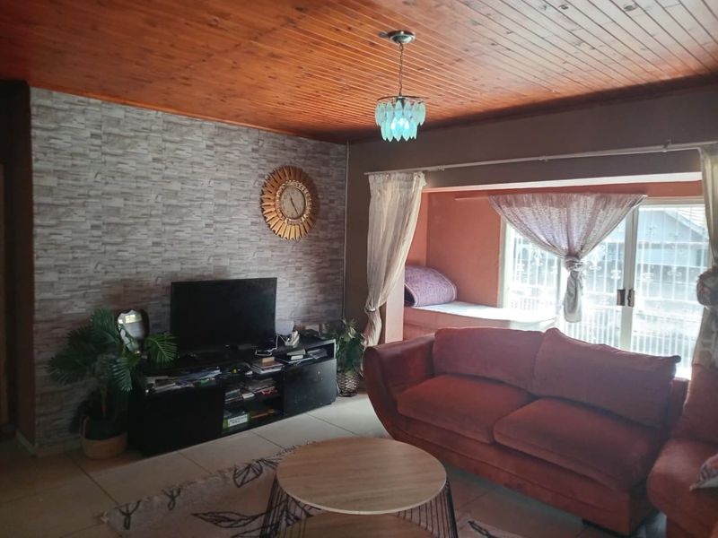 A living room featuring a timber tongue and groove ceiling, tiled flooring, and a stone-effect feature wall with access to an outdoor area.
