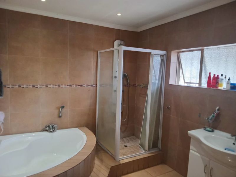 A functional bathroom featuring a corner bathtub, a separate shower enclosure, and a vanity basin with tiled finishes throughout.