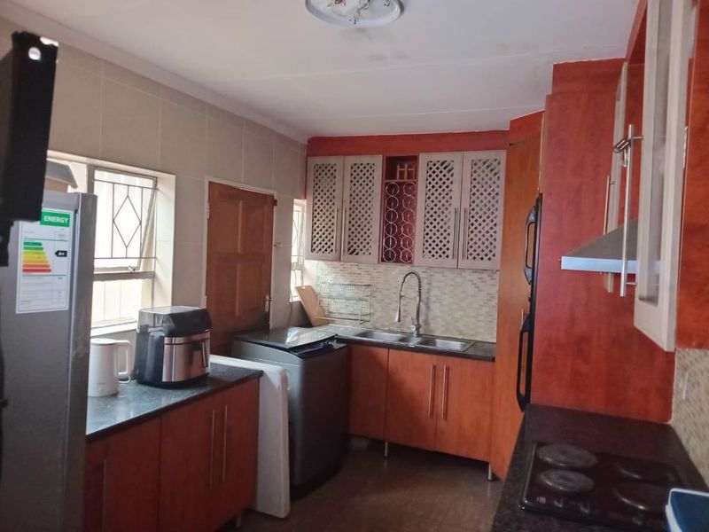 A functional kitchen featuring built-in cabinetry, a double sink, tiled backsplash, and integrated cooking appliances, with security bars on the windows.