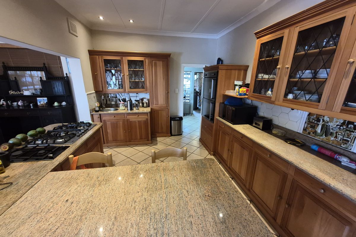 Spacious kitchen featuring warm wooden cabinetry, granite countertops, a central island with a gas hob, and integrated built-in oven.