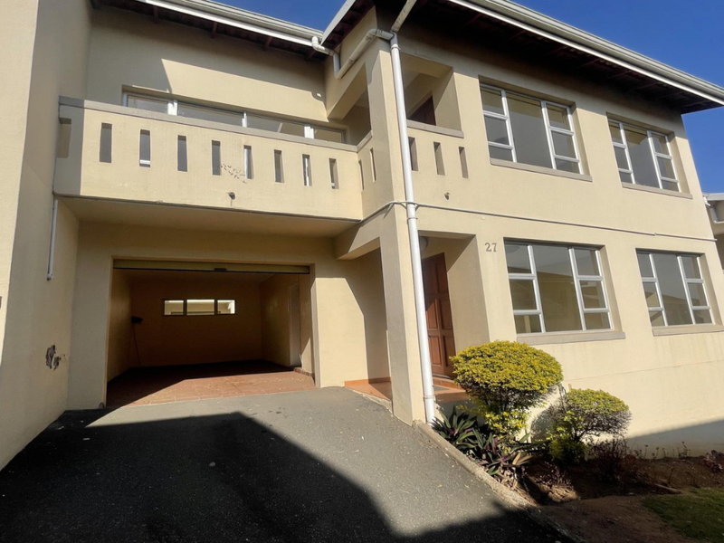 Front elevation of a two-story townhouse featuring a built-in garage, upper-level balcony, and paved driveway access.