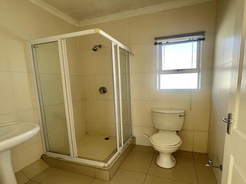 A functional bathroom featuring a pedestal basin, a corner shower enclosure, and a toilet, finished with neutral wall and floor tiles.