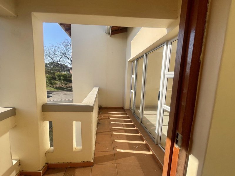 A covered balcony featuring tiled flooring and sliding glass doors, providing an outdoor transition space with a masonry balustrade.