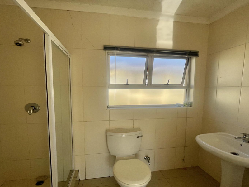 A functional bathroom featuring a shower enclosure, pedestal basin, and toilet, with tiled finishes throughout. The space is ready for modernization.