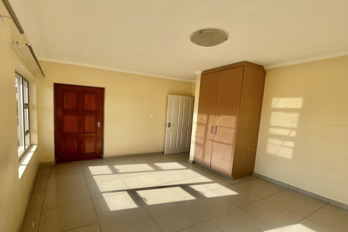 A bright, empty bedroom featuring tiled flooring, a built-in wardrobe, and natural light through aluminium-framed windows.