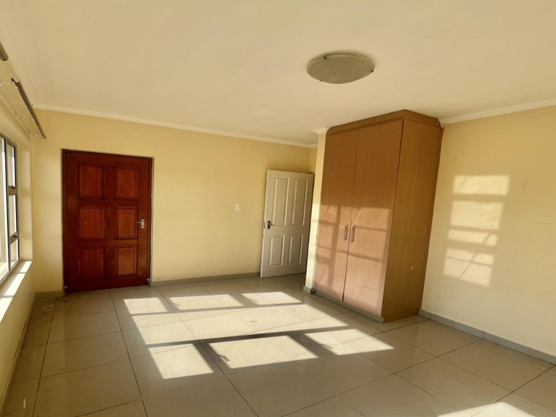 A bright, empty bedroom featuring tiled flooring, a built-in wardrobe, and natural light through aluminium-framed windows.