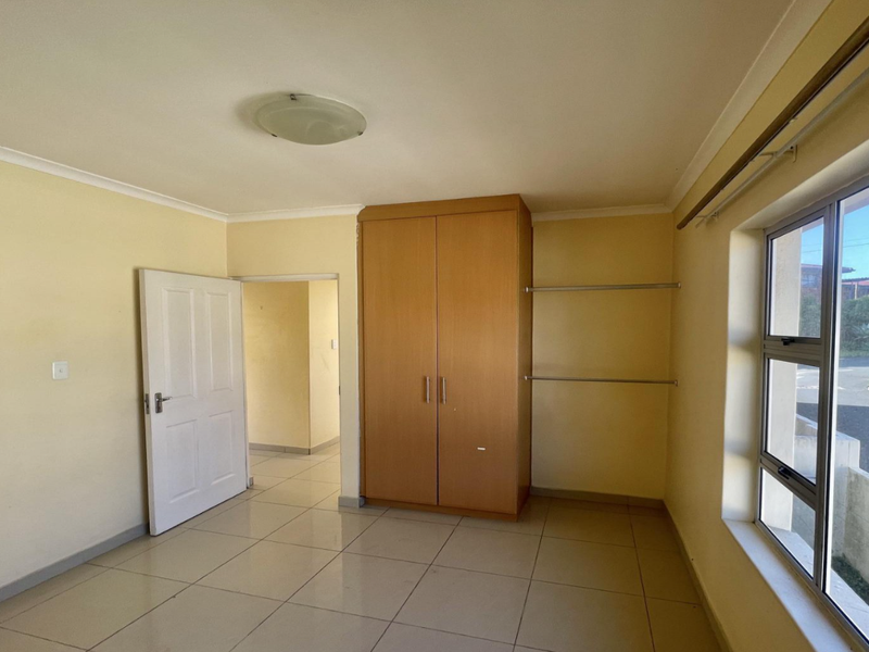 A bright, empty bedroom featuring tiled flooring, a built-in wardrobe, and large windows providing natural light and exterior views.