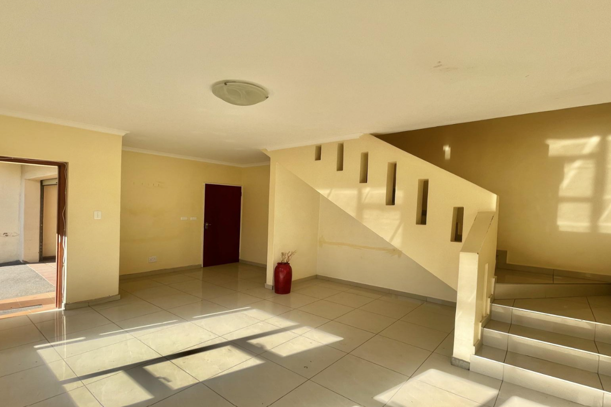 An empty, open-plan living area featuring tiled flooring and a staircase, providing a blank canvas for renovation and interior design.