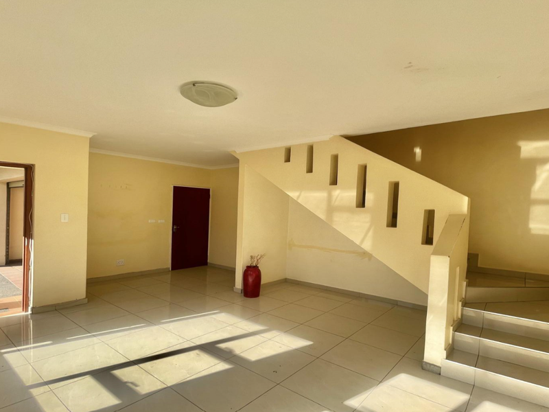 An empty, open-plan living area featuring tiled flooring and a staircase, providing a blank canvas for renovation and interior design.