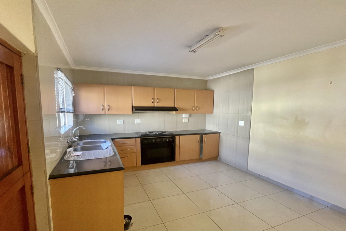 A functional kitchen featuring built-in cabinetry, a stainless steel sink, and integrated oven and hob, with tiled flooring and splashbacks throughout.
