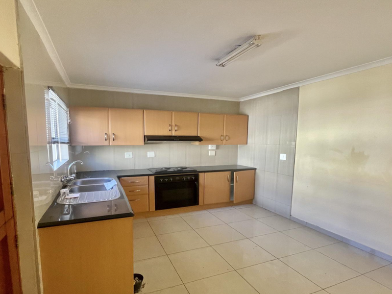 A functional kitchen featuring built-in cabinetry, a stainless steel sink, and integrated oven and hob, with tiled flooring and splashbacks throughout.