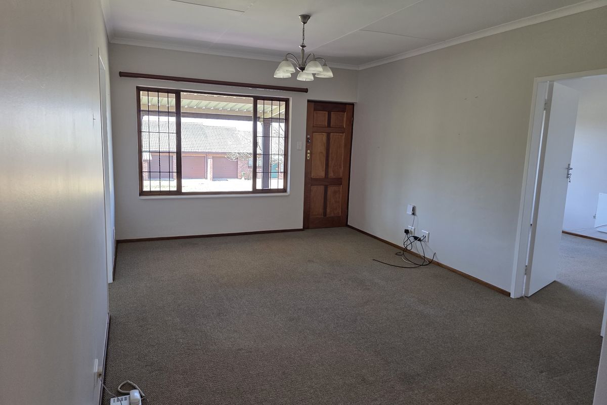An empty living room featuring carpet flooring, a timber entrance door, and a window with security bars, offering a blank canvas for personalization.