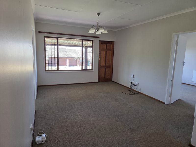 An empty living room featuring carpet flooring, a timber entrance door, and a window with security bars, offering a blank canvas for personalization.