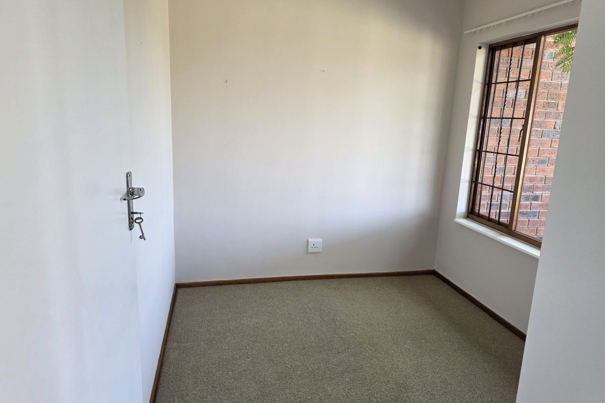 A vacant bedroom featuring neutral carpet flooring, timber-framed windows with security bars, and plain walls, offering a blank canvas for personalization.