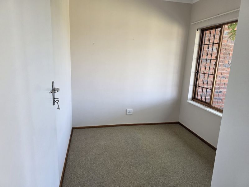 A vacant bedroom featuring neutral carpet flooring, timber-framed windows with security bars, and plain walls, offering a blank canvas for personalization.