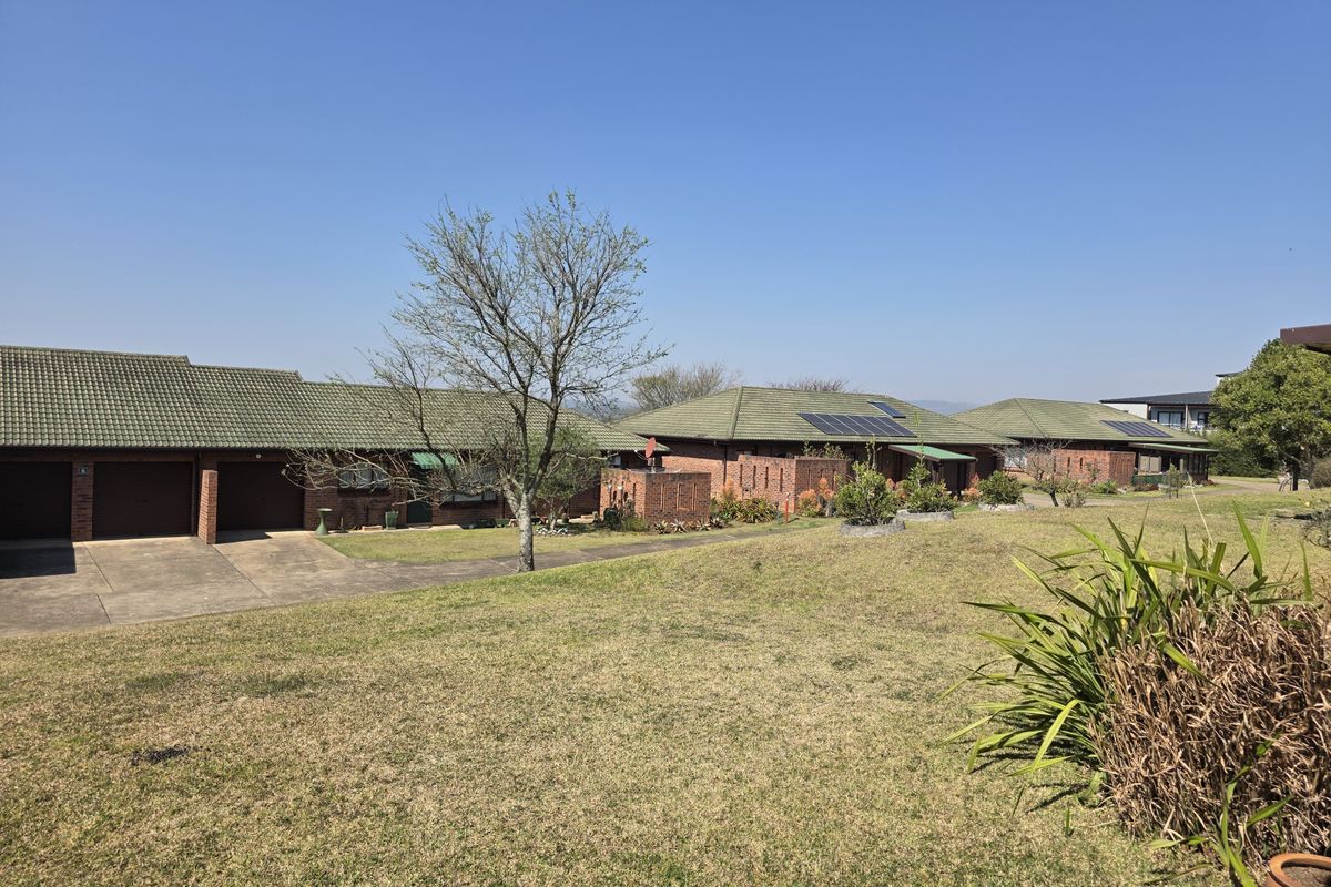 A view of the rear exterior of the retirement village units, featuring brick construction, tiled roofs, solar panels, and shared lawn areas.