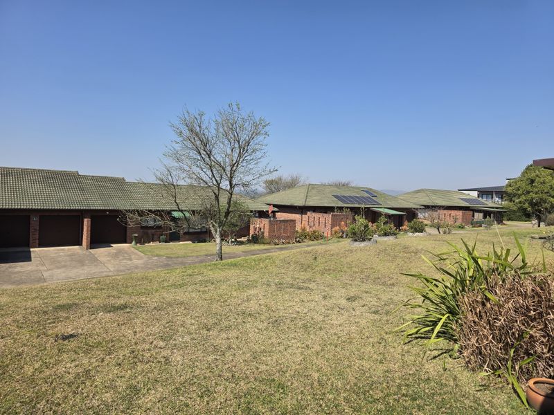 A view of the rear exterior of the retirement village units, featuring brick construction, tiled roofs, solar panels, and shared lawn areas.