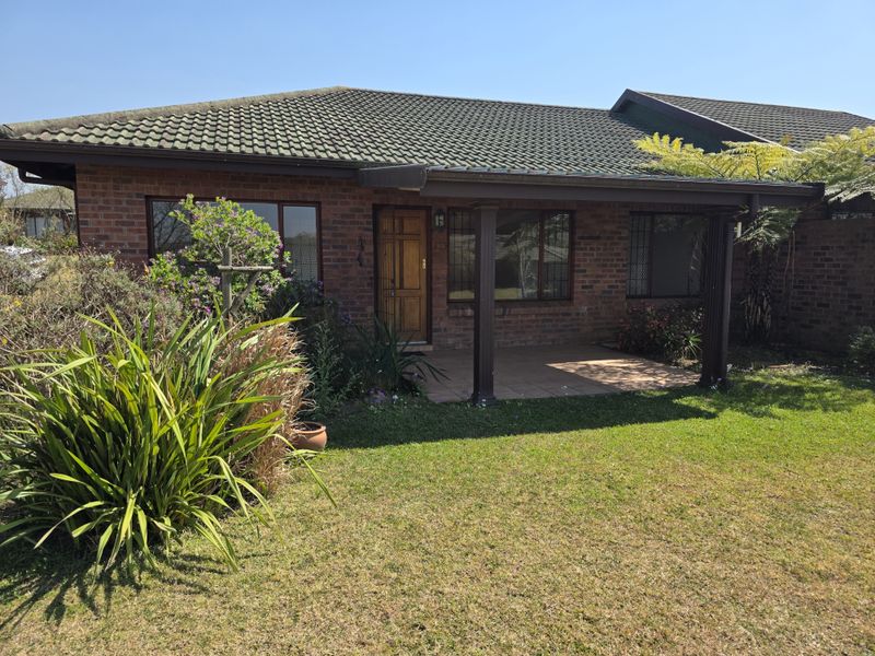 Front elevation of a brick retirement village unit featuring a covered patio entrance, tiled roof, and established garden surroundings.