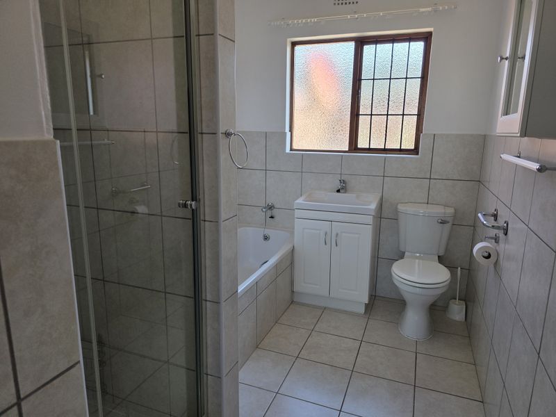 A clean, functional bathroom featuring a separate shower enclosure, built-in bathtub, vanity cabinet with basin, and toilet with neutral wall and floor tiling.