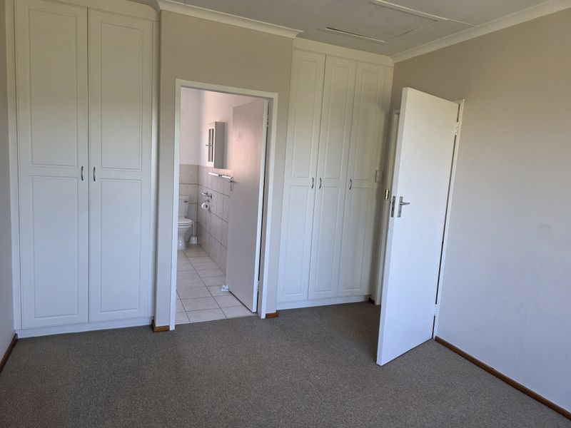 A clean, empty bedroom featuring neutral carpeting, ample built-in cupboard storage, and direct access to an en-suite bathroom.