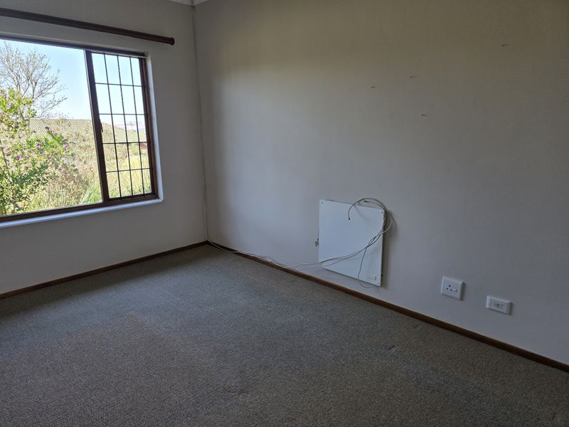 An empty bedroom featuring carpeted flooring, a large window with security bars, and a wall-mounted heater.