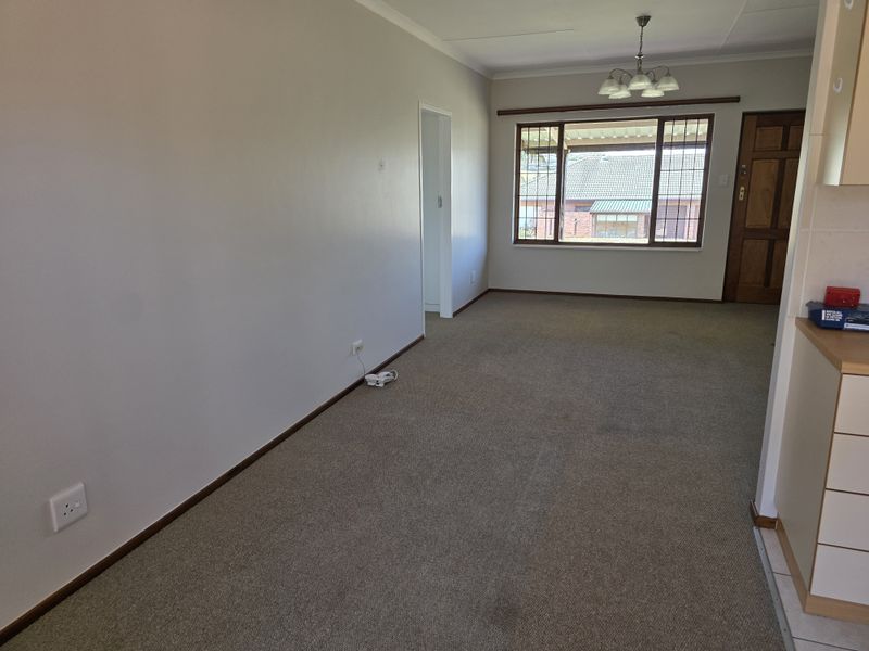 An empty open-plan living area featuring carpeted flooring, timber window frames, and a neutral color palette, ready for personalization.