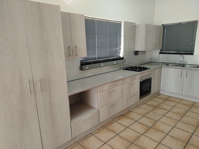 A clean, functional kitchen featuring light wood-tone cabinetry, stone-look laminate countertops, a gas hob, built-in oven, and tiled flooring throughout.