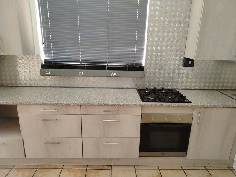 A functional kitchen area featuring light wood-finish cabinetry, granite countertops, a gas hob, built-in oven, and a durable metal splashback.