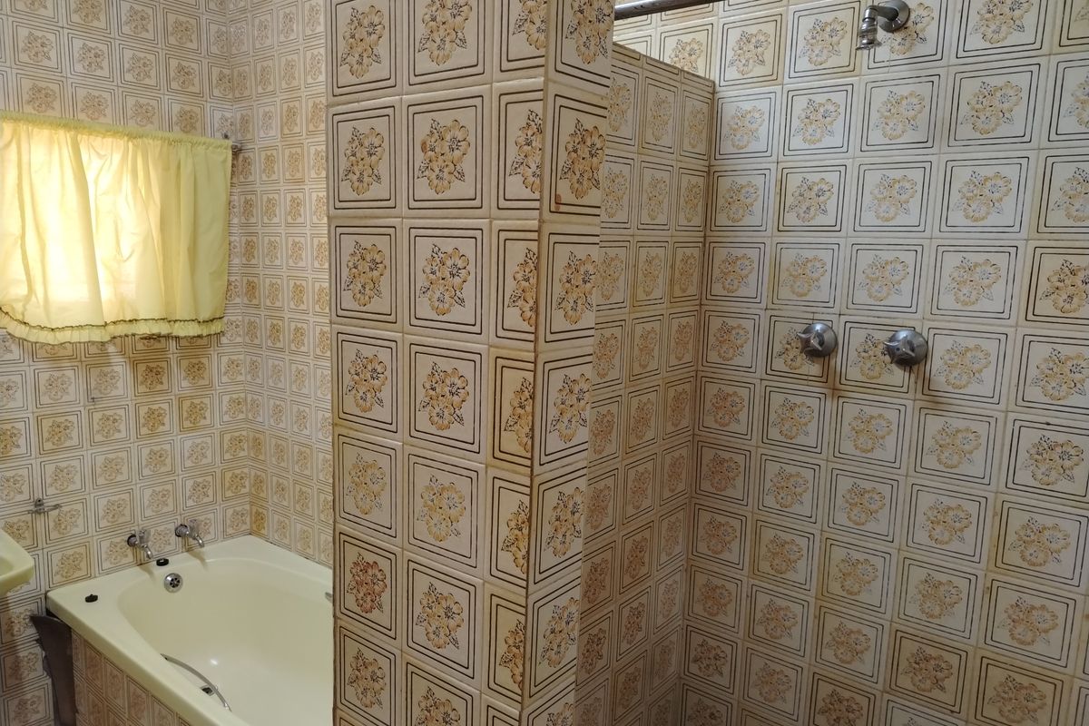A dated bathroom featuring a built-in bathtub and a separate shower area with vintage floral patterned wall tiles throughout.