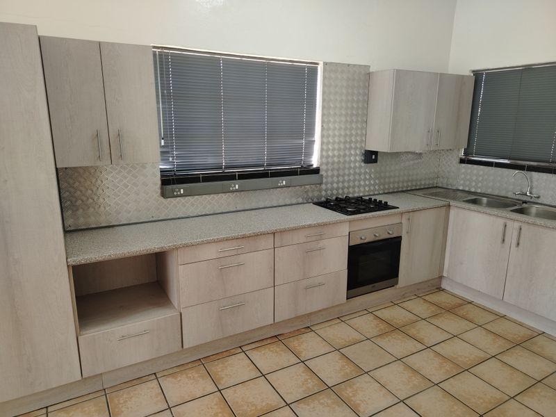 A functional kitchen featuring light wood-look cabinetry, granite-effect countertops, a gas hob, built-in oven, and tiled flooring with ample storage space.