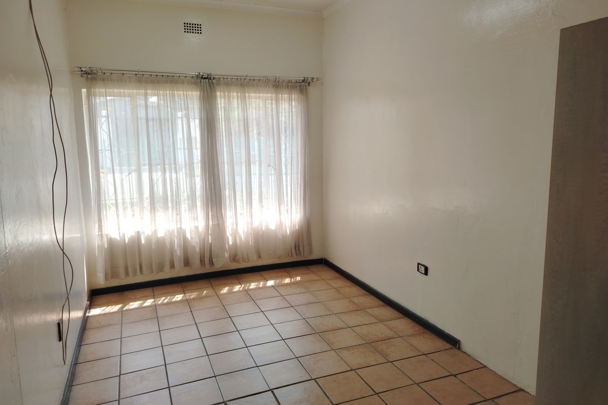 A vacant bedroom featuring tiled flooring, a large window with curtain rod, and neutral wall finishes, ready for personalization.