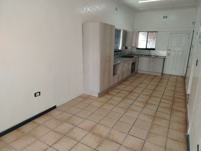 A functional, empty kitchen featuring light-toned built-in cabinetry, a built-in oven and hob, and tiled flooring throughout.