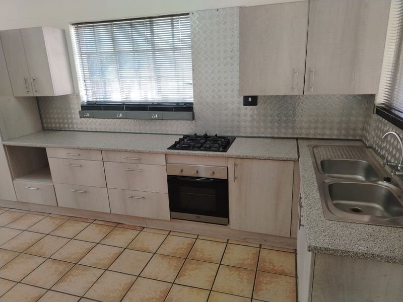A functional kitchen featuring light wood-tone cabinetry, a built-in gas hob and oven, metal splashbacks, and a double bowl sink with tiled flooring.