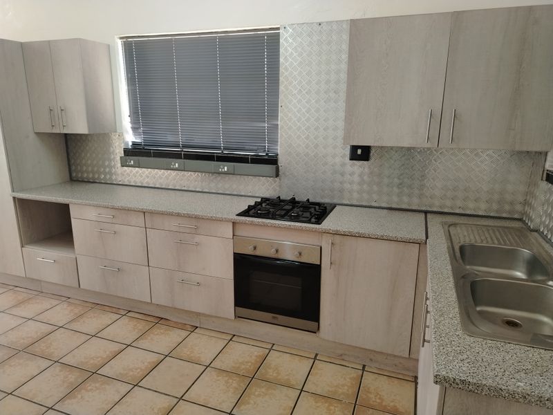 A functional kitchen featuring light wood-look cabinetry, granite-effect countertops, a gas hob with oven, and a stainless steel double sink with tiled flooring.
