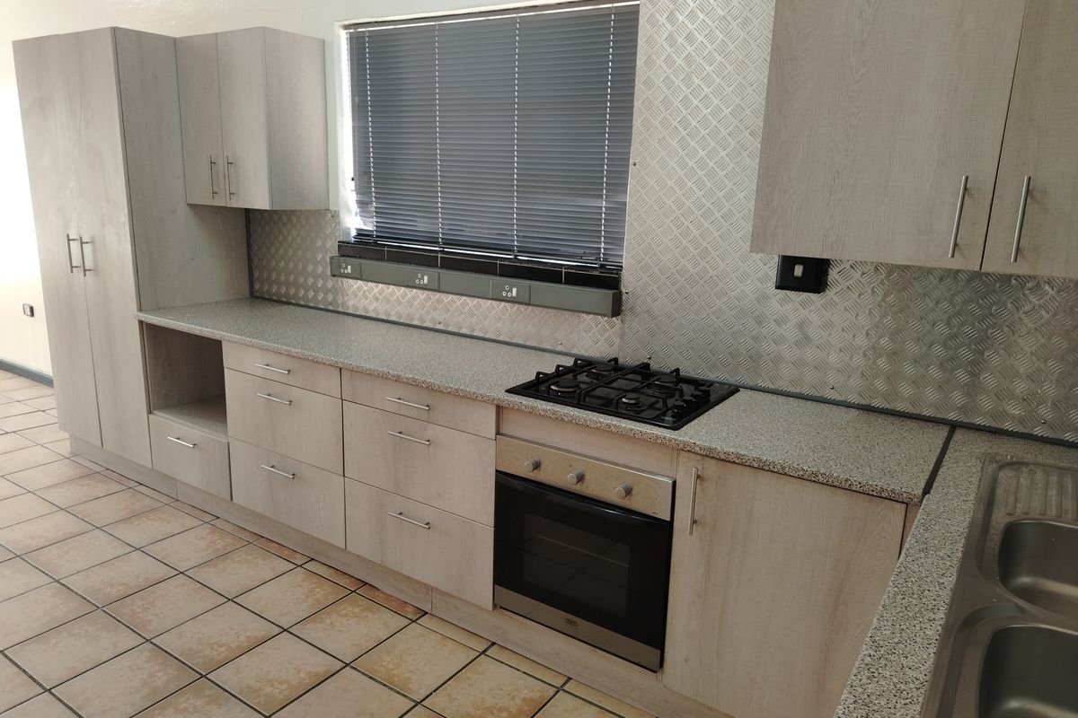 A clean, functional kitchen featuring light wood-tone cabinetry, granite-look countertops, a gas hob, built-in oven, and durable tiled flooring.