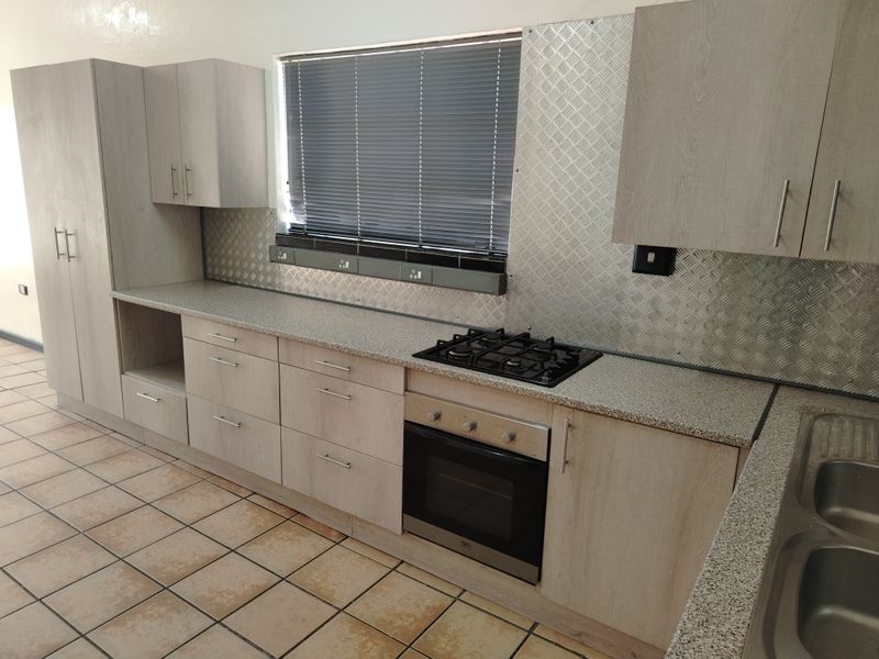 A clean, functional kitchen featuring light wood-tone cabinetry, granite-look countertops, a gas hob, built-in oven, and durable tiled flooring.
