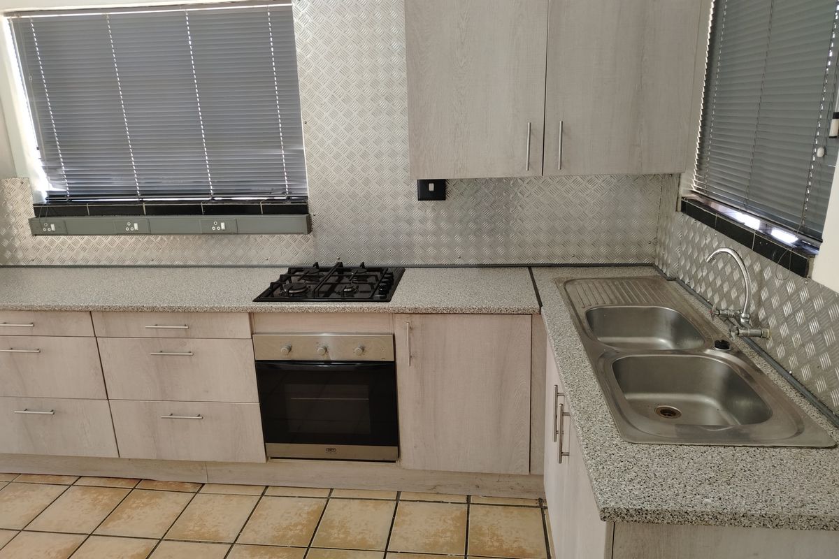 Functional kitchen featuring light wood-look cabinetry, a gas hob, built-in oven, double stainless steel sink, and durable metal splashback finishes.