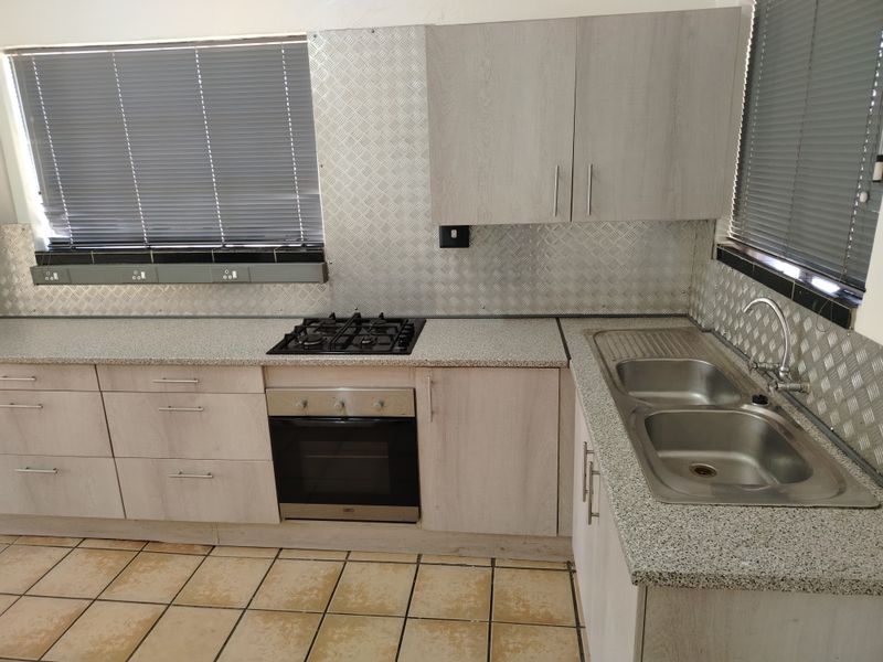 Functional kitchen featuring light wood-look cabinetry, a gas hob, built-in oven, double stainless steel sink, and durable metal splashback finishes.