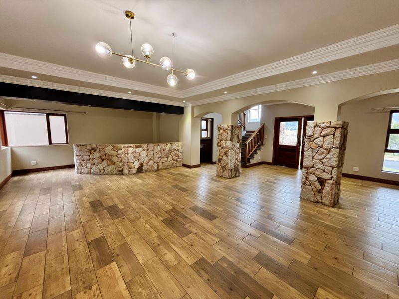 Spacious open-plan living area featuring stone-clad architectural columns, a built-in stone bar, wood-look tile flooring, and elegant crown molding throughout.