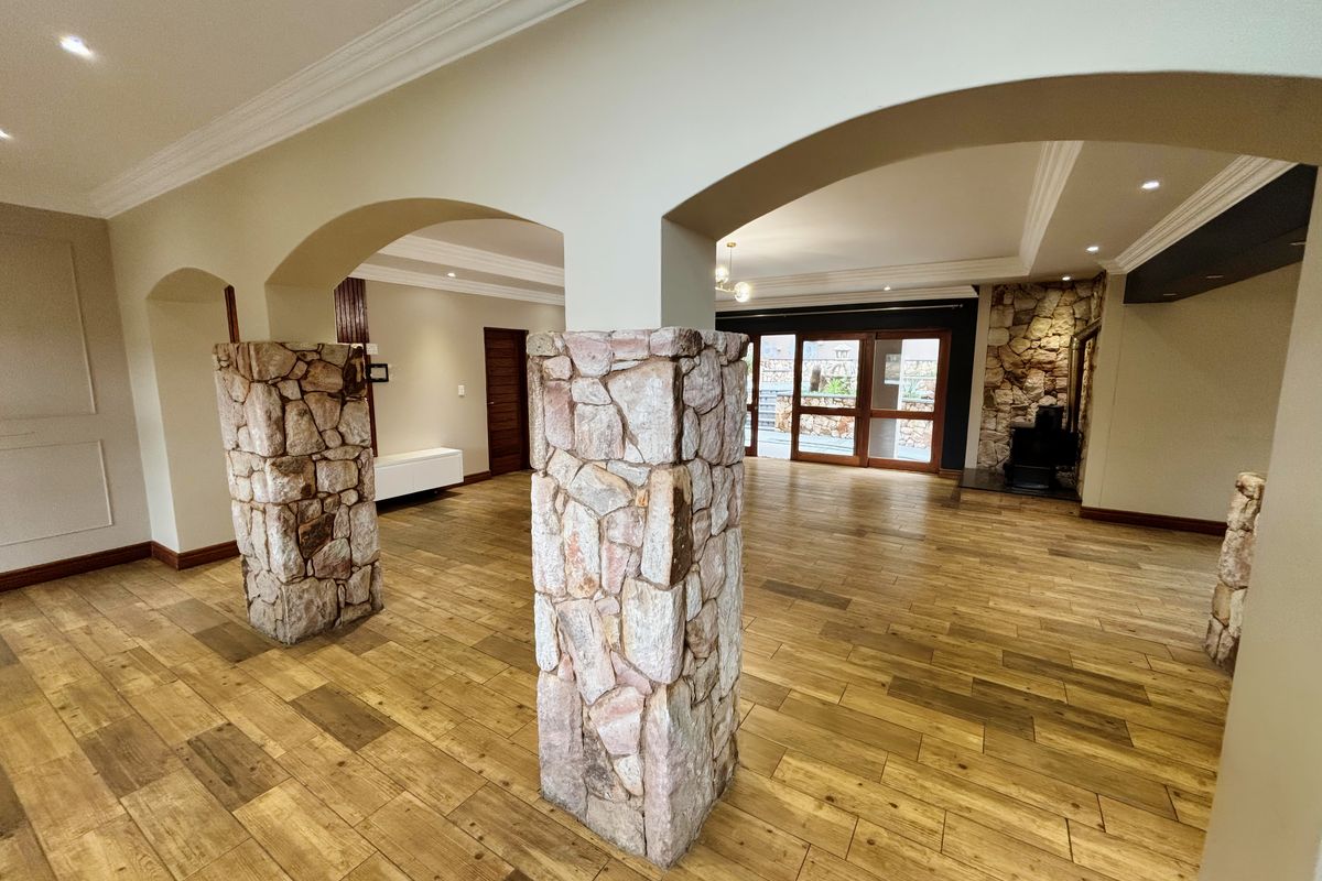 Spacious open-plan living area featuring distinctive stone-clad pillars, arched architectural details, wood-look tile flooring, and a cozy fireplace with access to the patio.