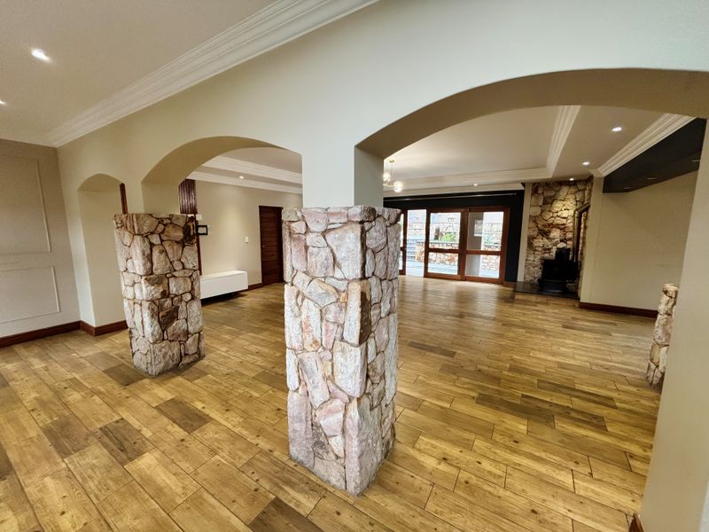 Spacious open-plan living area featuring distinctive stone-clad pillars, arched architectural details, wood-look tile flooring, and a cozy fireplace with access to the patio.